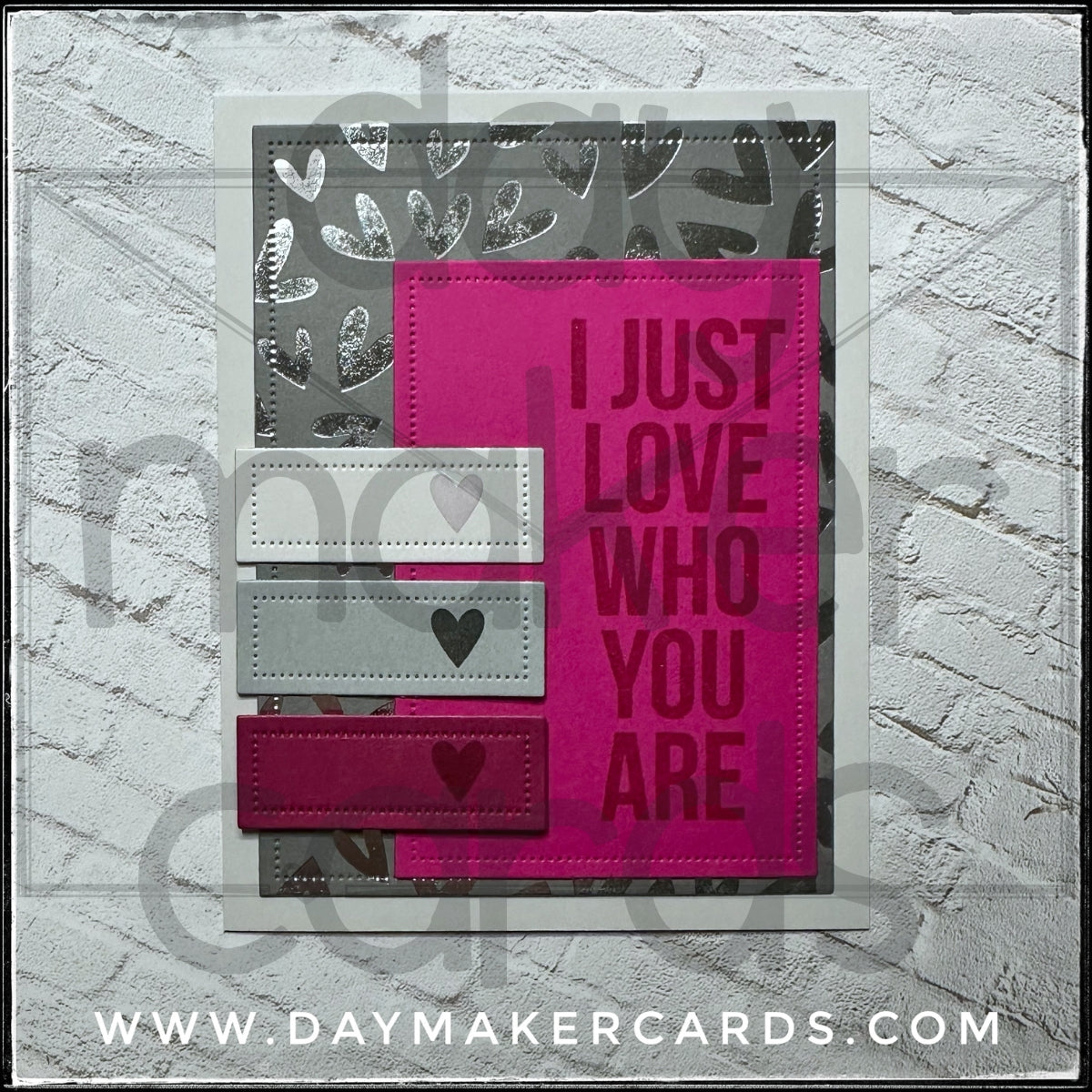 Handmade card from Day Maker Cards, stamped with 'I Just Love Who You Are' text on a pink background with heart designs, displayed against a silver foiled background.