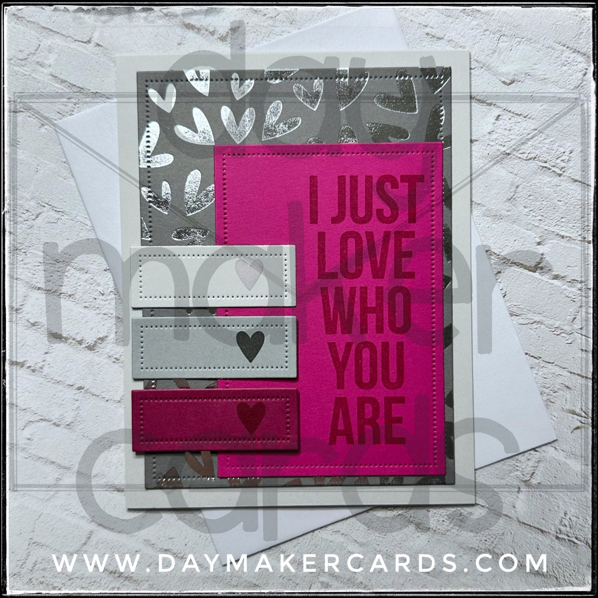 Handmade card from Day Maker Cards, stamped with 'I Just Love Who You Are' text on a pink background with heart designs, displayed against a silver foiled background.